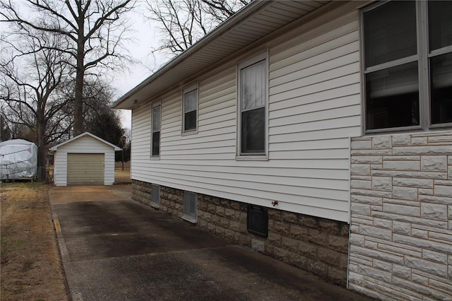 view of side of property featuring an outbuilding, stone siding, driveway, and a detached garage