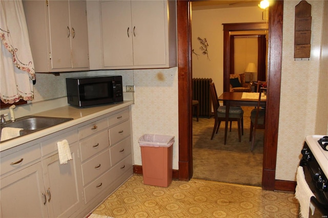 kitchen with light tile patterned floors, radiator, light countertops, black appliances, and a sink