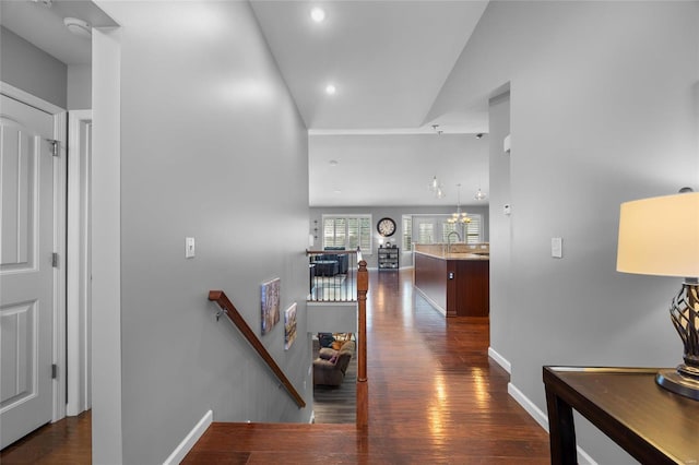 corridor featuring an inviting chandelier, dark wood-type flooring, a sink, an upstairs landing, and baseboards