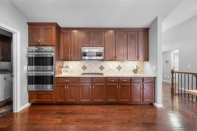 kitchen featuring backsplash, appliances with stainless steel finishes, dark wood-type flooring, washer / dryer, and baseboards