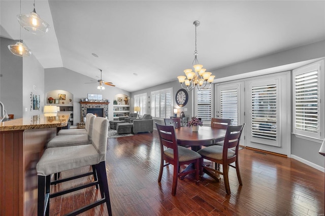 dining room featuring visible vents, dark wood-style floors, vaulted ceiling, a brick fireplace, and ceiling fan with notable chandelier