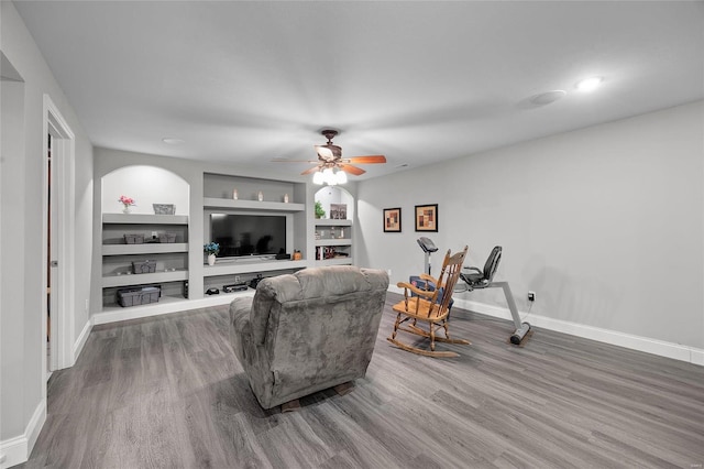 living area with baseboards, wood finished floors, a ceiling fan, and built in features