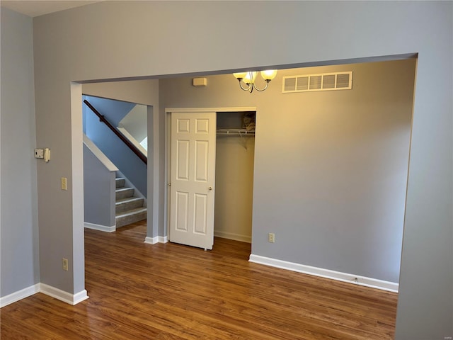 unfurnished bedroom featuring wood-type flooring, a notable chandelier, and a closet