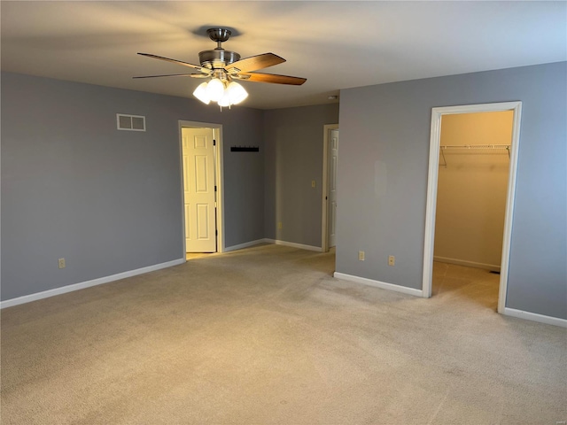 unfurnished bedroom with ceiling fan, a closet, a spacious closet, and light carpet