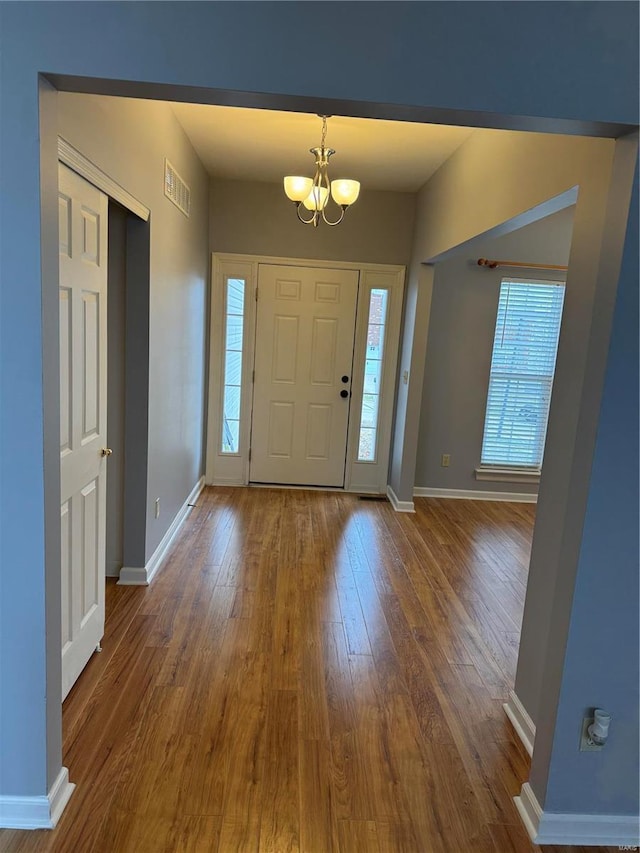 entrance foyer with a notable chandelier, baseboards, visible vents, and wood finished floors