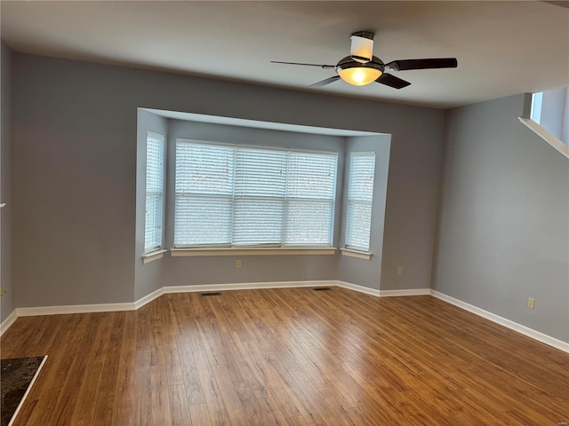 unfurnished room with a ceiling fan, wood-type flooring, visible vents, and baseboards