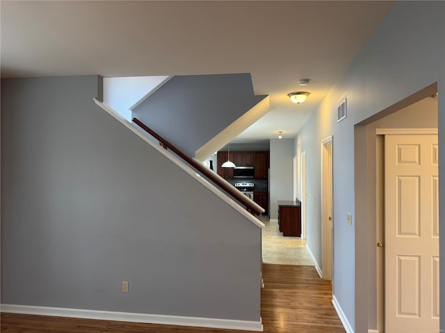 hallway featuring stairway, wood finished floors, visible vents, and baseboards