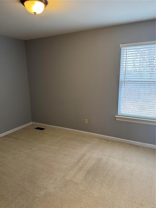 spare room featuring a healthy amount of sunlight, baseboards, visible vents, and light colored carpet