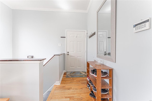 corridor featuring light wood finished floors, baseboards, ornamental molding, and an upstairs landing