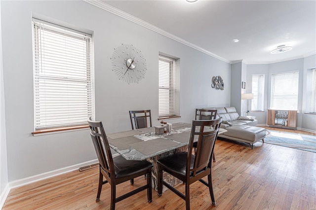 dining area with light wood-style floors, baseboards, ornamental molding, and a wealth of natural light