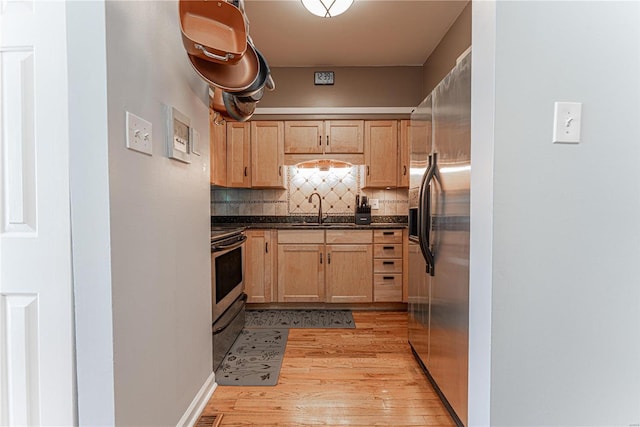 kitchen featuring dark countertops, light brown cabinets, appliances with stainless steel finishes, and a sink