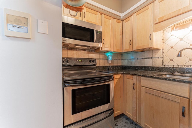 kitchen featuring stainless steel appliances, a sink, backsplash, and light brown cabinetry