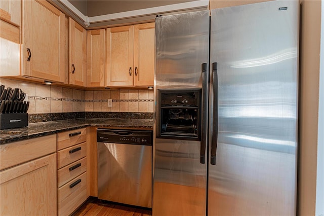 kitchen with stainless steel appliances, dark stone counters, light brown cabinets, and decorative backsplash