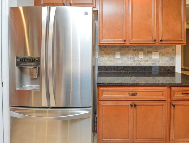 kitchen with stainless steel fridge with ice dispenser, decorative backsplash, and dark stone counters