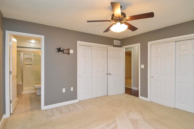 unfurnished bedroom with ceiling fan, ensuite bath, light carpet, and two closets