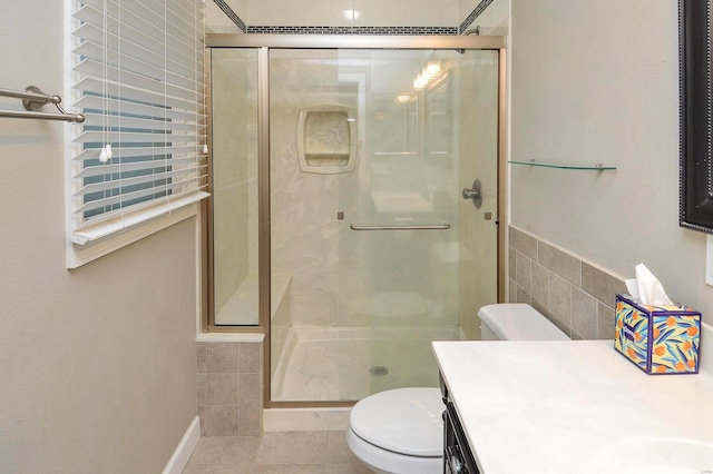 bathroom featuring a shower with door, tile walls, vanity, tile patterned floors, and toilet