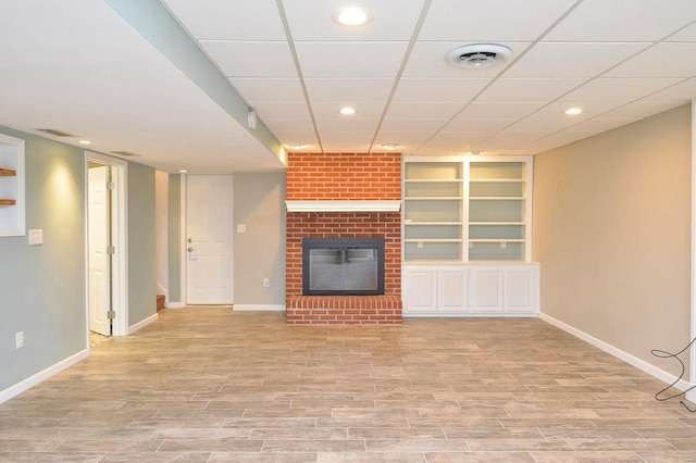 unfurnished living room with built in shelves, a fireplace, and light hardwood / wood-style floors