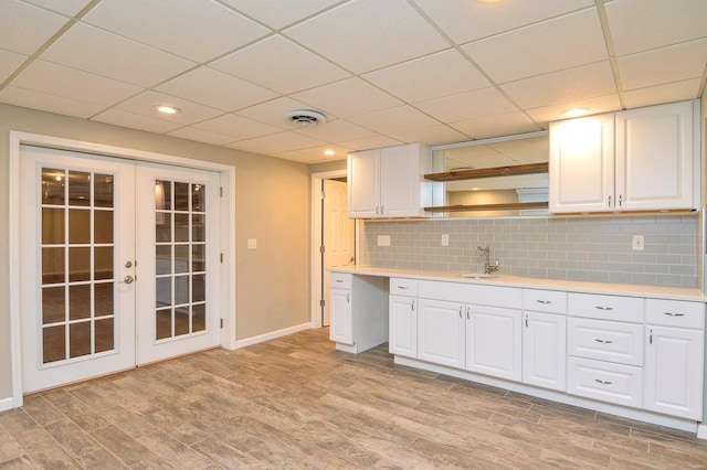 kitchen with sink, white cabinetry, backsplash, light hardwood / wood-style floors, and french doors