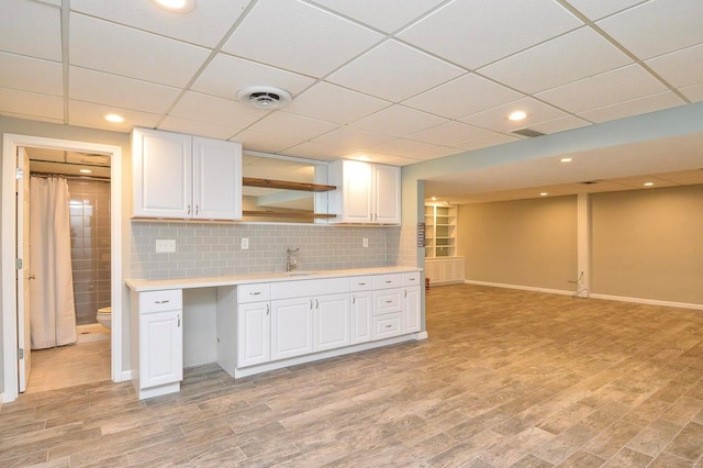 kitchen featuring sink, a paneled ceiling, white cabinetry, light hardwood / wood-style floors, and decorative backsplash