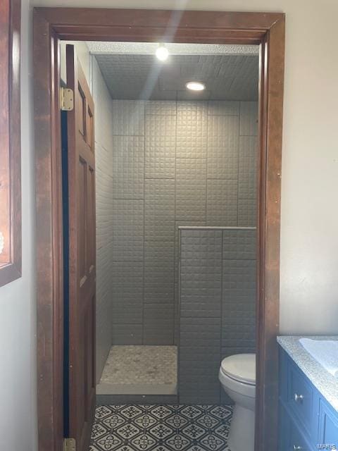 bathroom with tile patterned flooring, vanity, toilet, and a tile shower