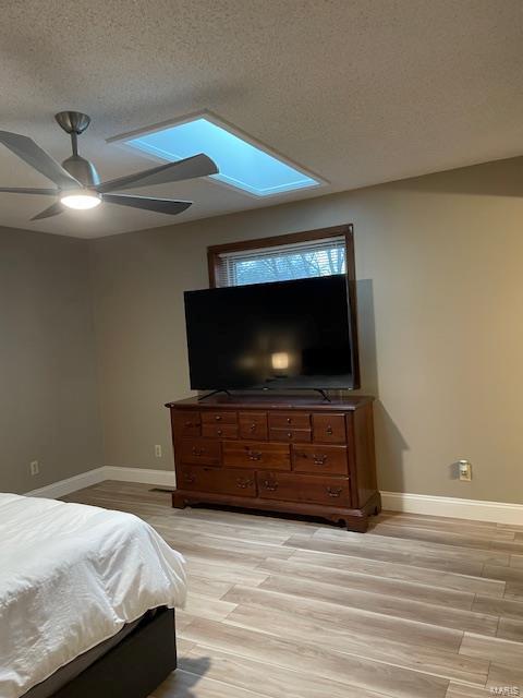 bedroom featuring ceiling fan, a skylight, a textured ceiling, and light wood-type flooring