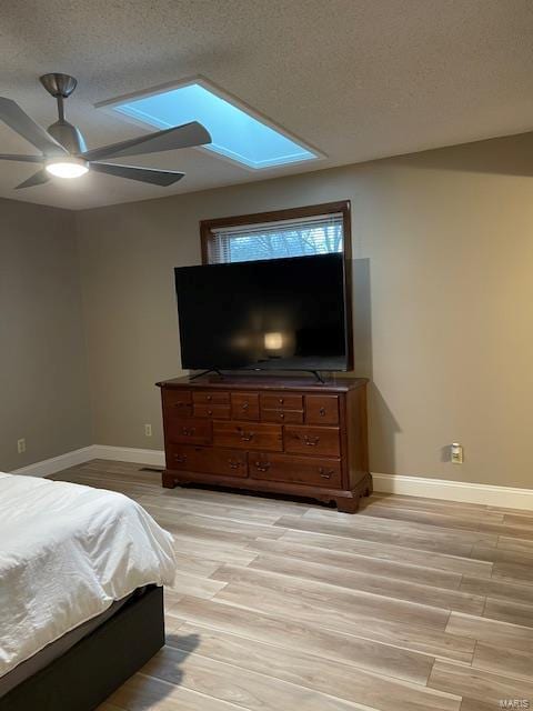 bedroom with ceiling fan, a skylight, light hardwood / wood-style flooring, and a textured ceiling