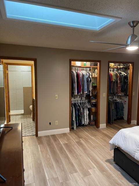 bedroom featuring connected bathroom, light hardwood / wood-style floors, multiple closets, and ceiling fan