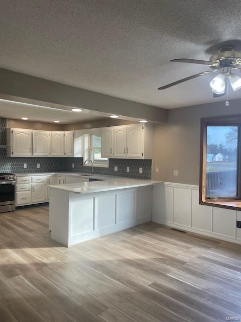 kitchen featuring sink, stainless steel range with electric cooktop, light hardwood / wood-style flooring, kitchen peninsula, and white cabinets