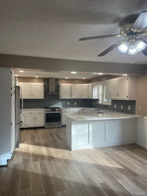 kitchen featuring wall chimney exhaust hood, white cabinetry, appliances with stainless steel finishes, and kitchen peninsula