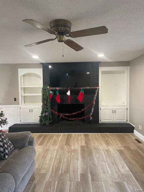 living room with built in shelves, a textured ceiling, light wood-type flooring, ceiling fan, and a fireplace