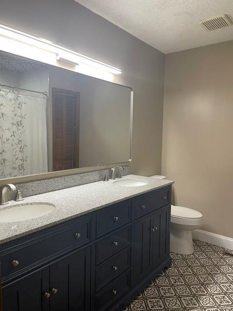 bathroom featuring tile patterned flooring, vanity, a textured ceiling, and toilet