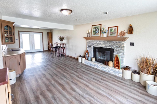 living room featuring french doors, a textured ceiling, a brick fireplace, and hardwood / wood-style flooring