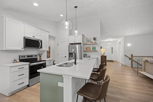 kitchen featuring sink, white cabinetry, hanging light fixtures, stainless steel appliances, and a kitchen island with sink