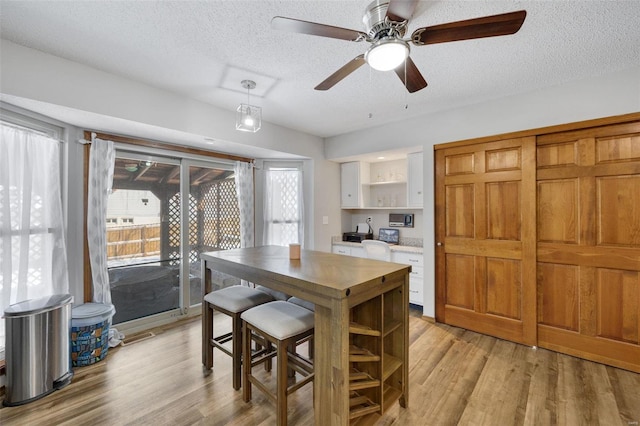 dining space with light wood-style floors, a textured ceiling, and a ceiling fan