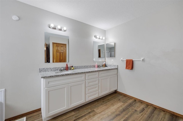 bathroom featuring double vanity, a sink, a textured ceiling, and wood finished floors