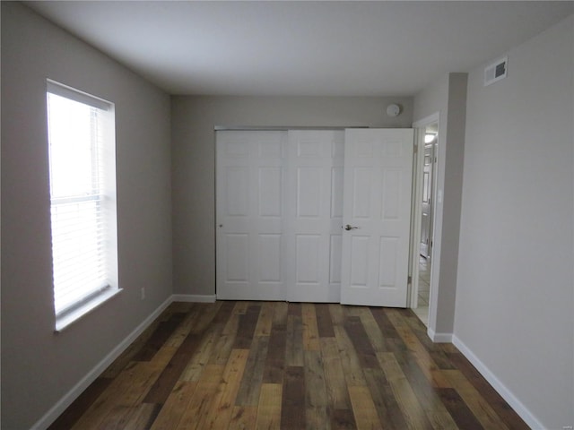 unfurnished bedroom featuring multiple windows, dark hardwood / wood-style flooring, and a closet