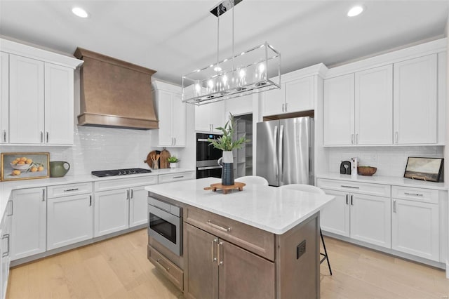 kitchen featuring white cabinetry, custom exhaust hood, stainless steel appliances, and light wood-style flooring