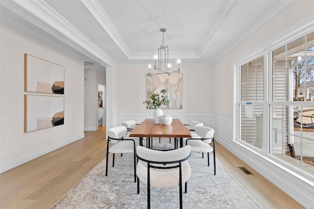 dining area featuring visible vents, a raised ceiling, wainscoting, wood finished floors, and an inviting chandelier