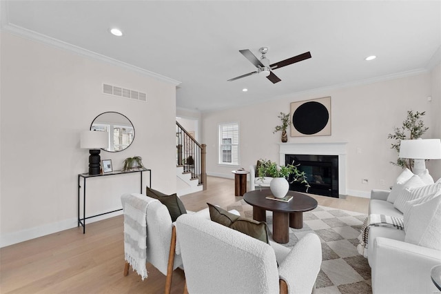 living room with light wood-type flooring, stairway, visible vents, and ornamental molding