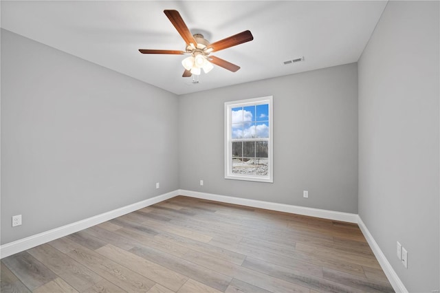 empty room with light wood finished floors, a ceiling fan, visible vents, and baseboards