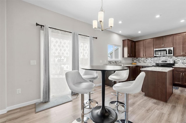 kitchen featuring backsplash, a center island, stainless steel appliances, light wood-style floors, and an inviting chandelier