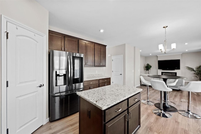 kitchen with light wood-type flooring, open floor plan, dark brown cabinetry, stainless steel fridge with ice dispenser, and hanging light fixtures