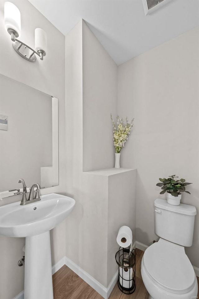 bathroom with visible vents, baseboards, toilet, wood finished floors, and a sink