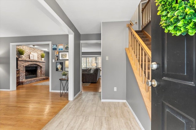 foyer featuring stairs, a brick fireplace, baseboards, and light wood-type flooring