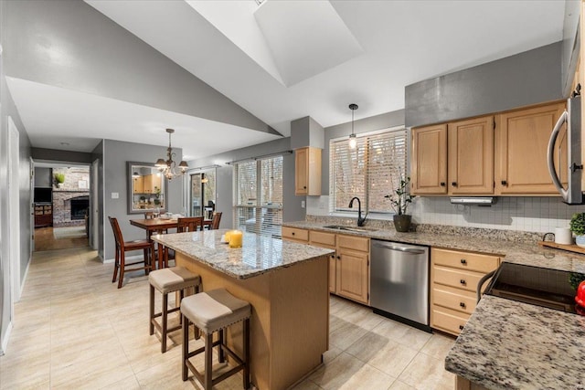 kitchen with light brown cabinets, lofted ceiling, a sink, appliances with stainless steel finishes, and a center island