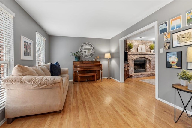 living area with a brick fireplace, light wood-style flooring, and baseboards