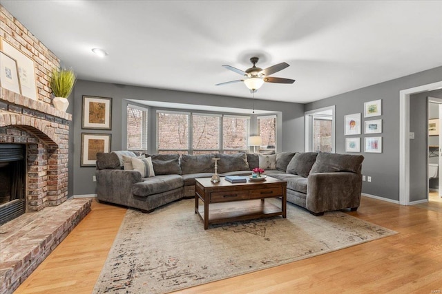 living room featuring ceiling fan, a brick fireplace, baseboards, and wood finished floors