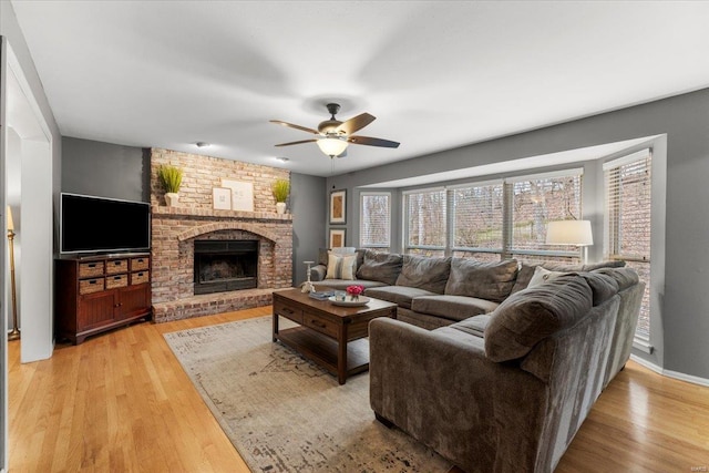 living room featuring a ceiling fan, a brick fireplace, and light wood-style floors