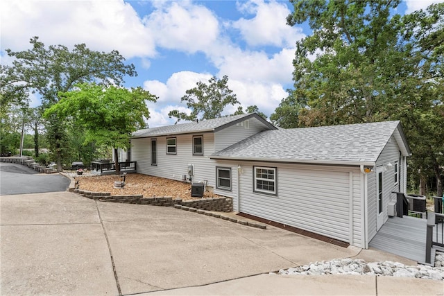 exterior space with central AC, roof with shingles, a wooden deck, and driveway