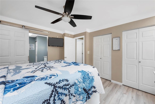 bedroom featuring light wood finished floors, a barn door, baseboards, ceiling fan, and two closets